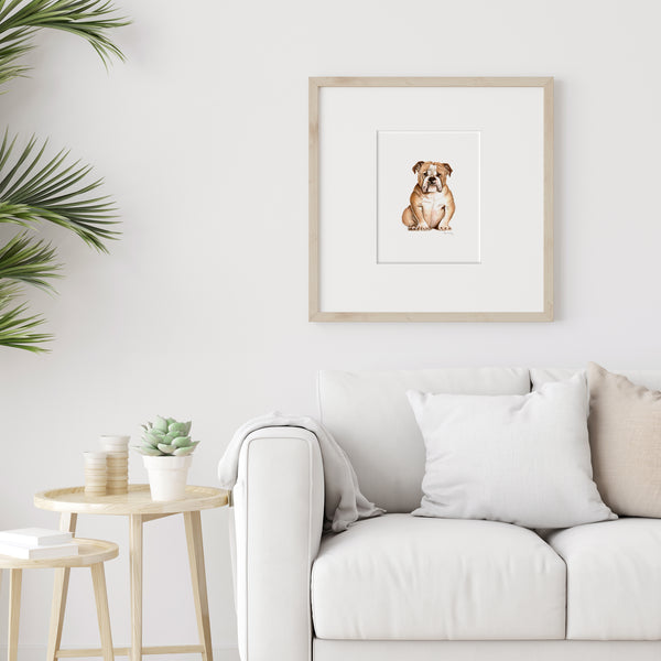 Watercolor painting of a tan bulldog in a wood frame on a wall over a white couch.