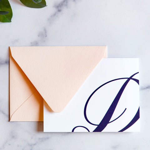 Monogram stationery with single script "D" bleeding off the card with a blush envelope on a marble table top.