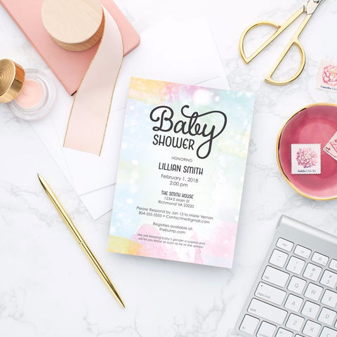 Rainbow watercolor textured baby shower invitation with gold pen and pink desk accessories.