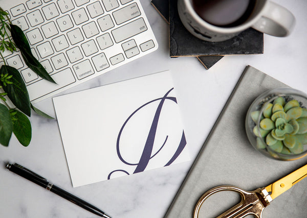 script monogram "D" notecard on desk with Apple keyboard, a succulent, gold scissors, a pen, and a cup of coffee.