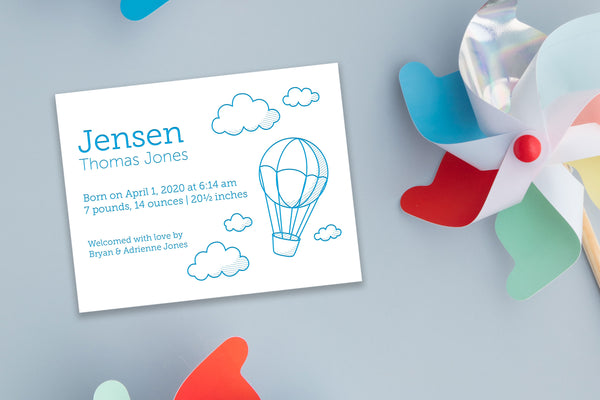 letterpress birth announcement with cloud and hot air balloon drawing in blue ink; colorful pinwheels in background