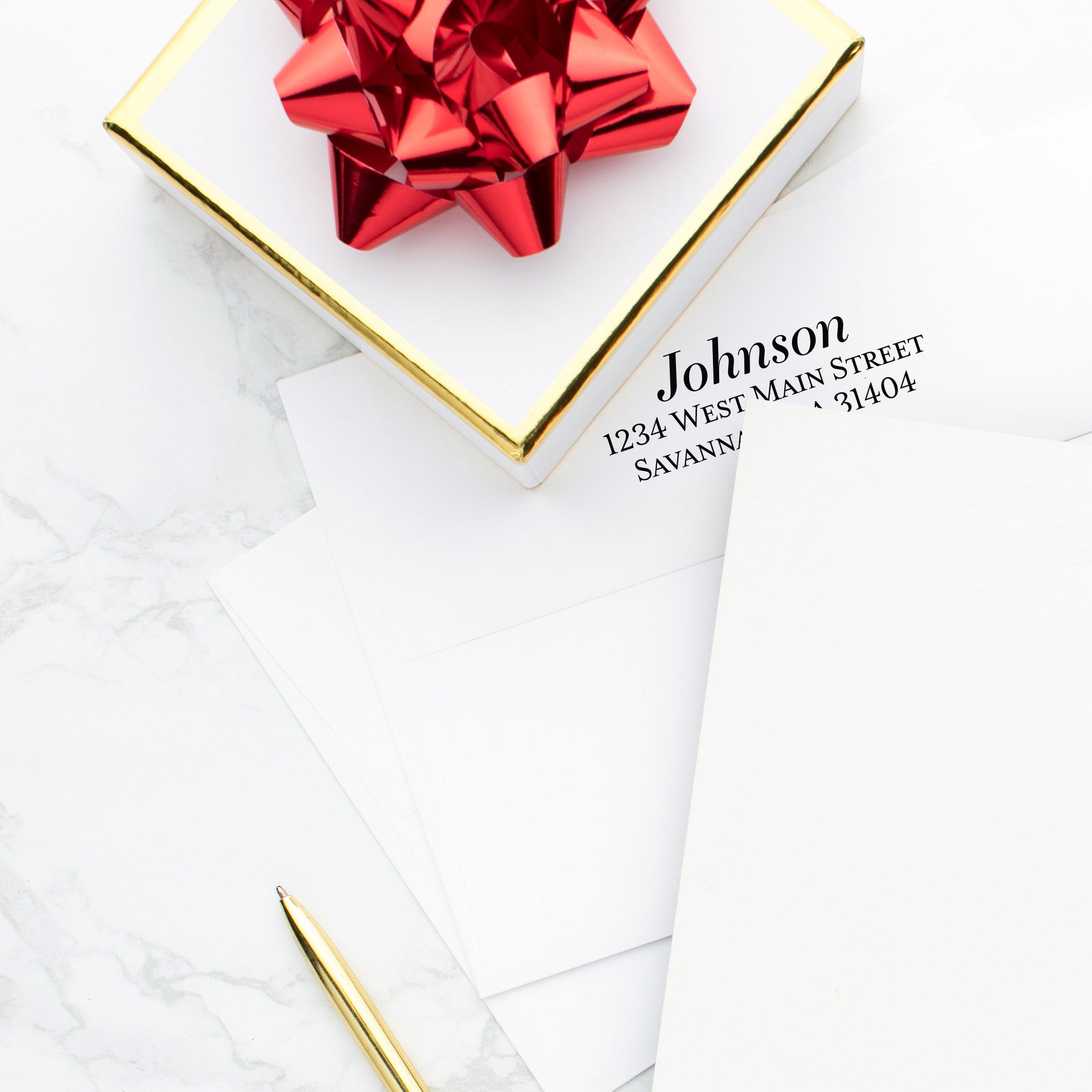 Classic serif font for envelope imprinting on white envelope with gold box and red holiday bow on desk.