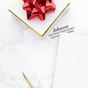 Classic serif font for envelope imprinting on white envelope with gold box and red holiday bow on desk.