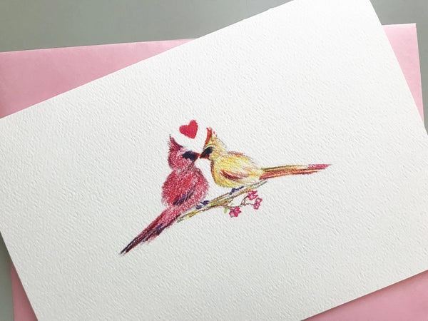 Detail view of colored pencil drawing of cardinals kissing with a heart on greeting card with pink envelope.