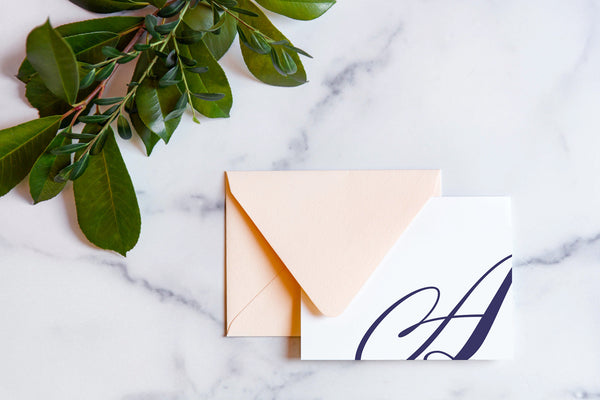 Monogram stationery with single script "A" bleeding off the card with a blush envelope on a marble table top.