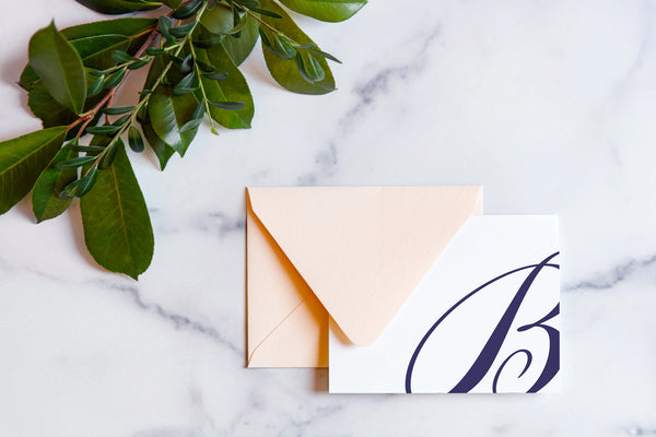 Monogram stationery with single script "B" bleeding off the card with a blush envelope on a marble table top.