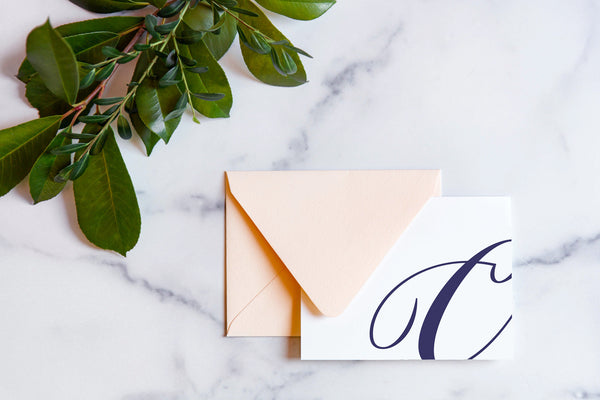 Monogram stationery with single script "C" bleeding off the card with a blush envelope on a marble table top.