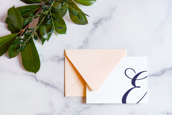 Monogram stationery with single script "E" bleeding off the card with a blush envelope on a marble table top.