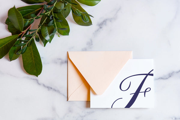 Monogram stationery with single script "F" bleeding off the card with a blush envelope on a marble table top.