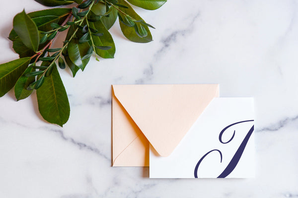 Monogram stationery with single script "I" bleeding off the card with a blush envelope on a marble table top.