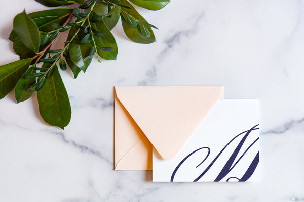 Monogram stationery with single script "M" bleeding off the card with a blush envelope on a marble table top.