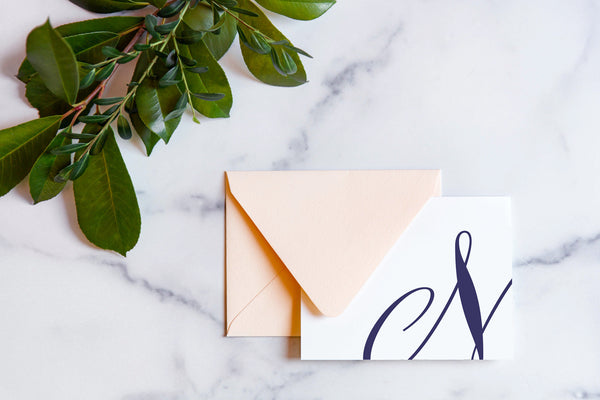 Monogram stationery with single script "N" bleeding off the card with a blush envelope on a marble table top.