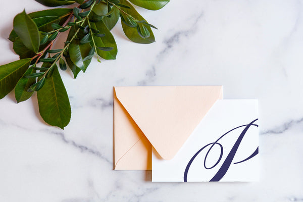 Monogram stationery with single script "P" bleeding off the card with a blush envelope on a marble table top.