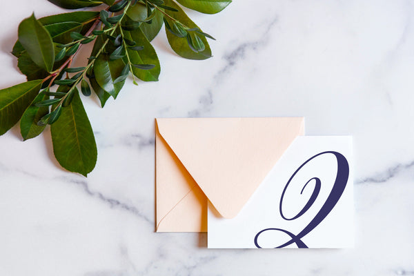 Monogram stationery with single script "Q" bleeding off the card with a blush envelope on a marble table top.