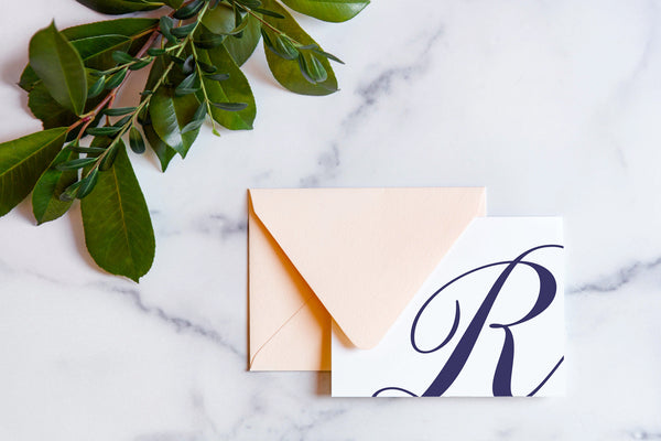 Monogram stationery with single script "R" bleeding off the card with a blush envelope on a marble table top.