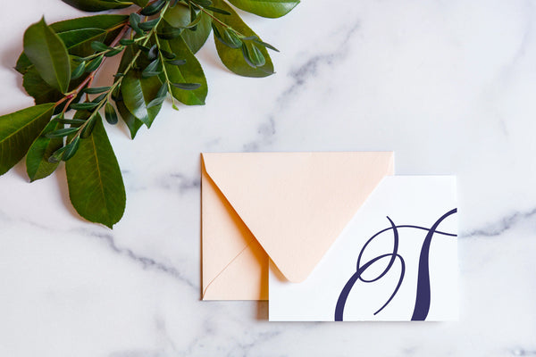 Monogram stationery with single script "S" bleeding off the card with a blush envelope on a marble table top.