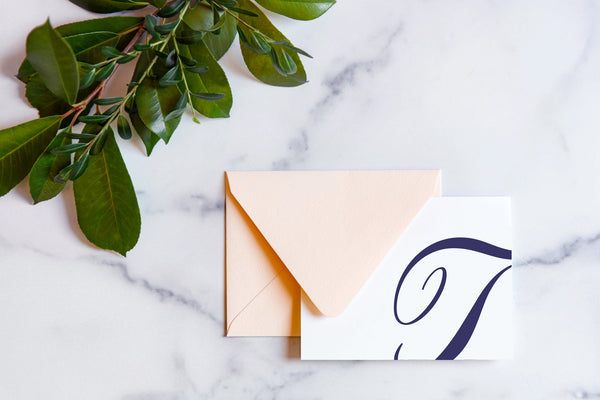 Monogram stationery with single script "T" bleeding off the card with a blush envelope on a marble table top.