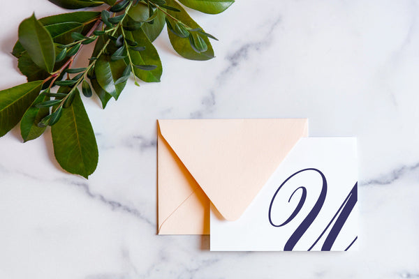 Monogram stationery with single script "U" bleeding off the card with a blush envelope on a marble table top.