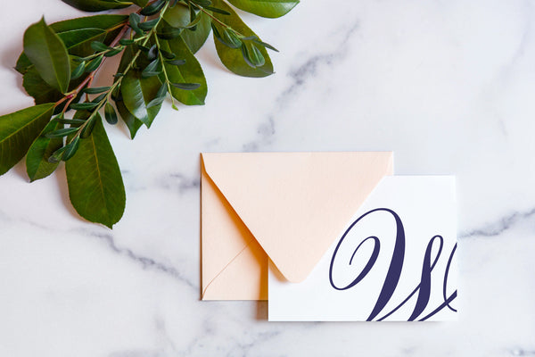 Monogram stationery with single script "W" bleeding off the card with a blush envelope on a marble table top.