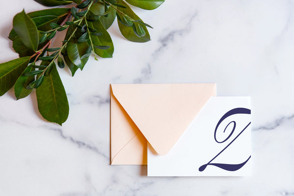 Monogram stationery with single script "Z" bleeding off the card with a blush envelope on a marble table top.