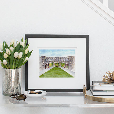 Art print of original watercolor painting of Virginia Tech Torgersen Bridge in black frame on entryway table with white tulips in a vase.